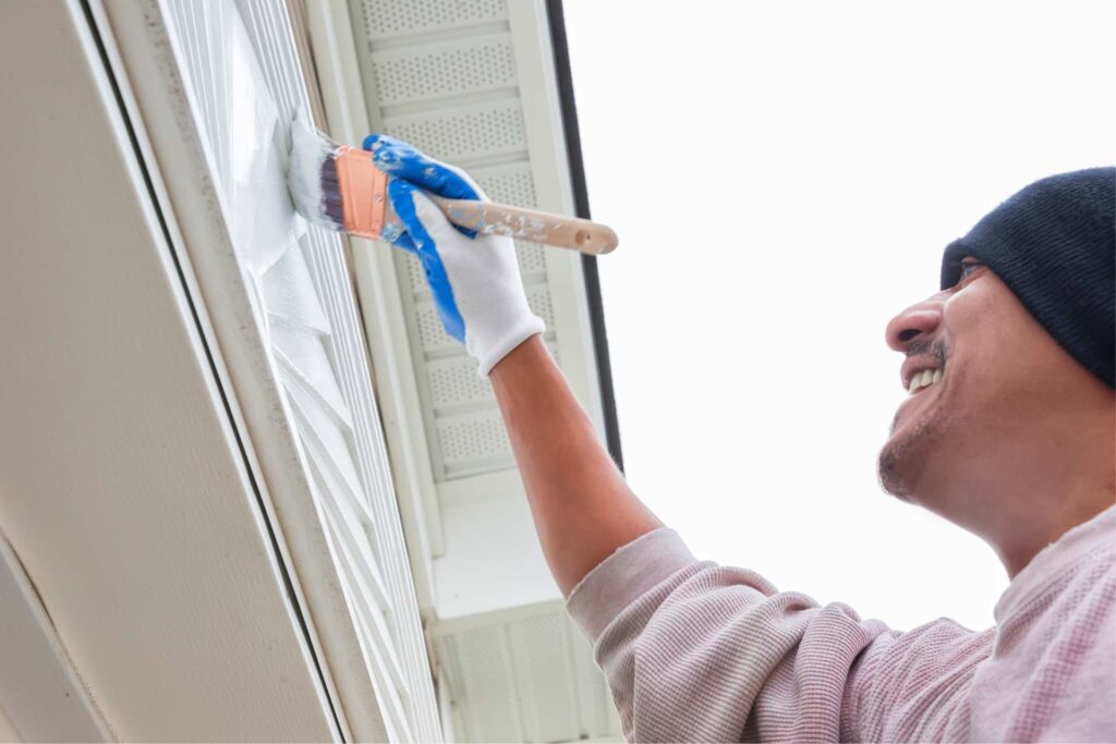 Maalari maalaamassa talon ulkoseinää valkoisella maalilla.