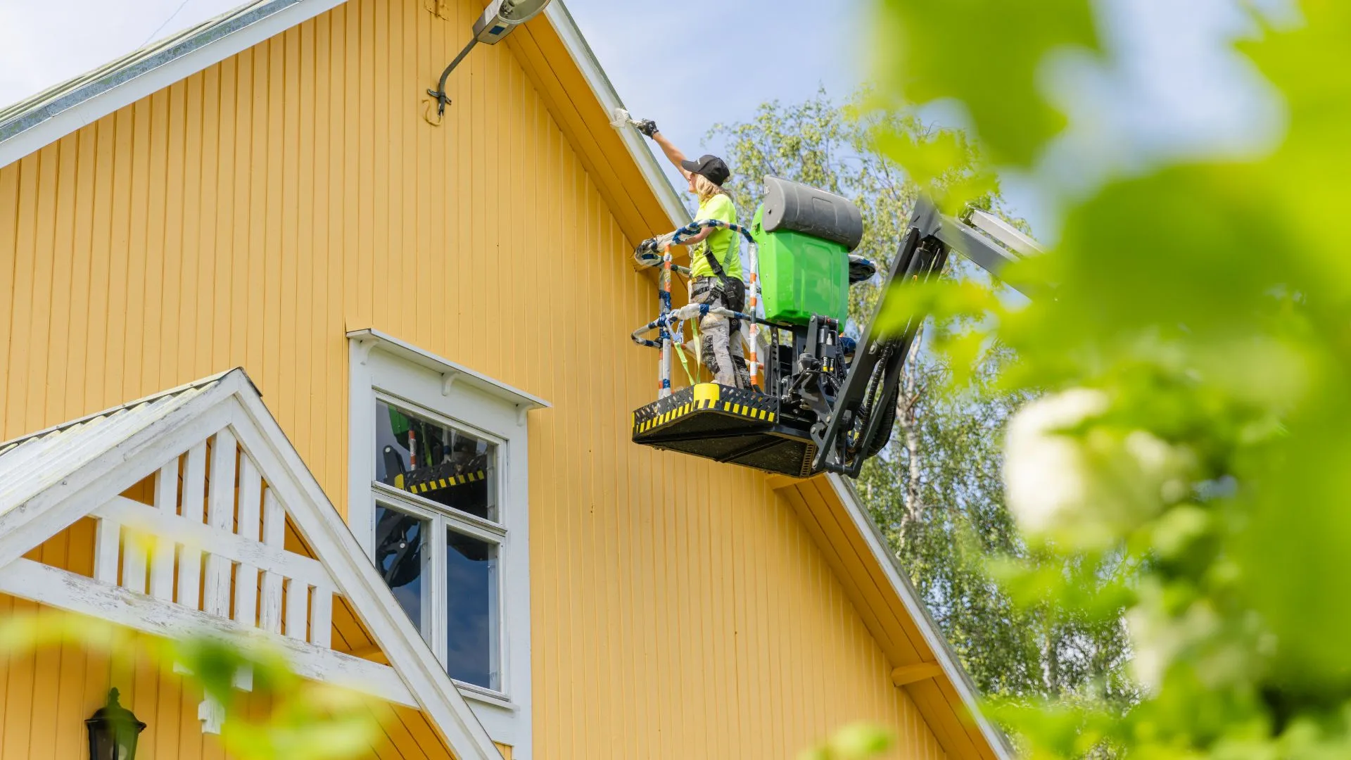 Keltaisen puutalon maalaustyö nostimesta käsin